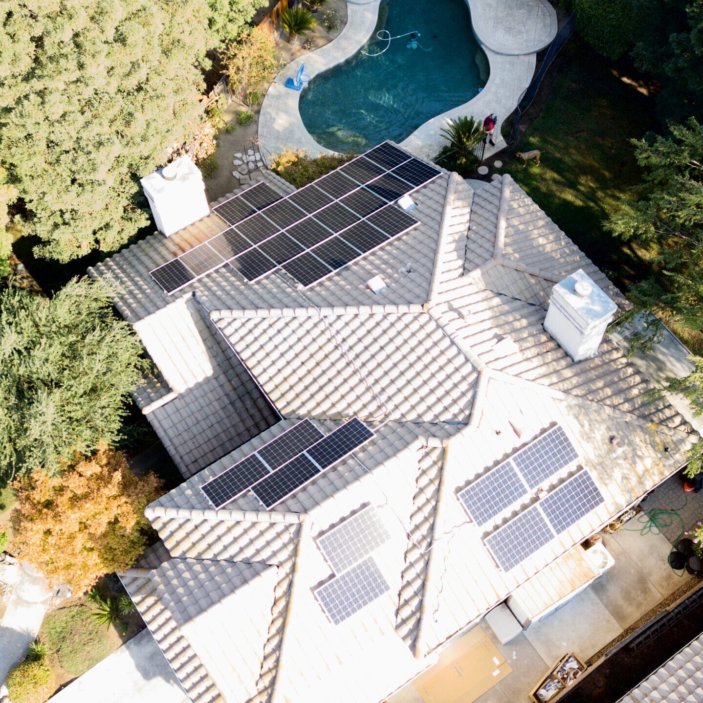 Areal view ofsolar panels and back yard with pool, trees, and surrounding area.