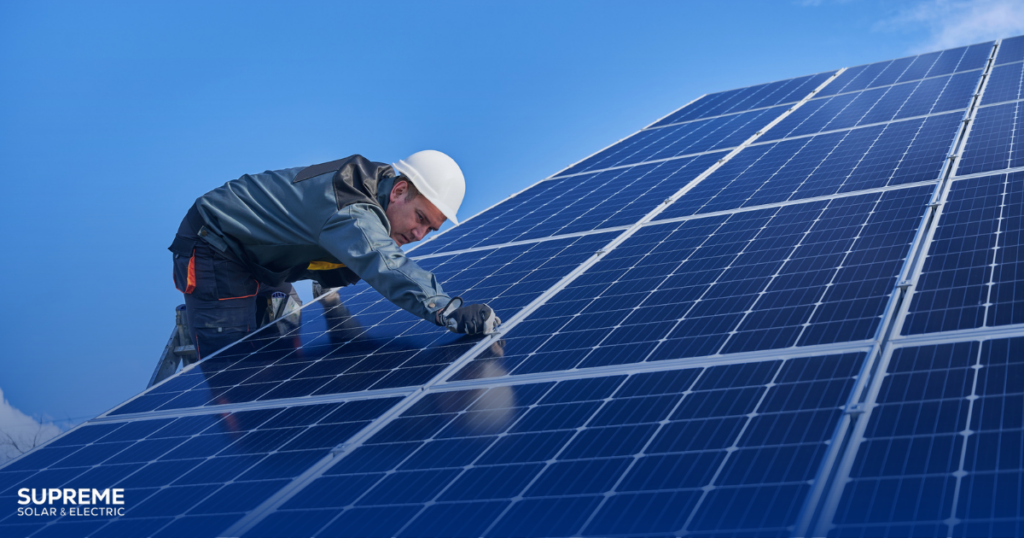 The Latest Solar Panel Technology in 2025 - a solar technician wears a hard hat and checks the solar panels he is working on.