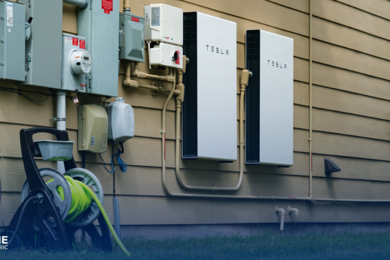 Most Popular Solar Battery Options: A Tesla Powerwall Battery is shown on the side of a house next to electrical boxes.