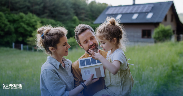 How to get started with solar - a couple with a youg daughter stand before their house with solar panels on the roof and hold a model of a house with solar panels
