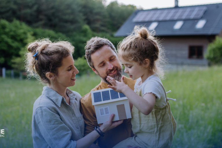 How to get started with solar - a couple with a youg daughter stand before their house with solar panels on the roof and hold a model of a house with solar panels