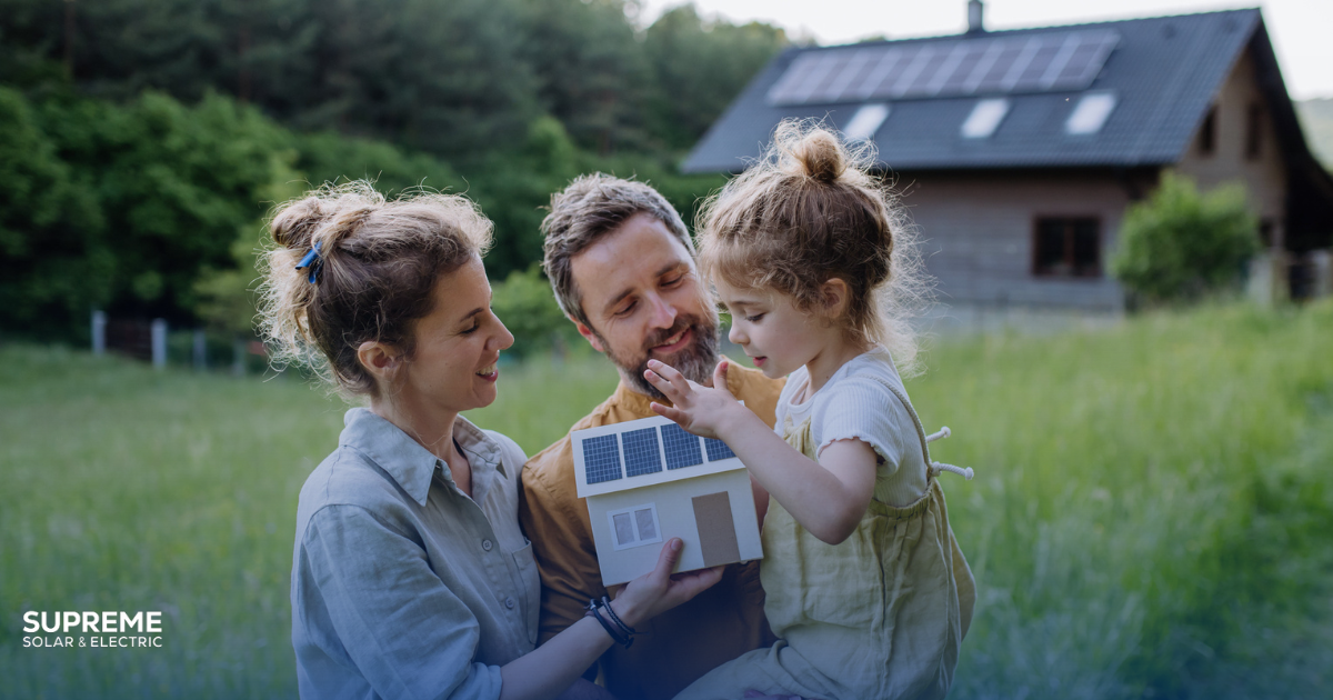 How to get started with solar - a couple with a youg daughter stand before their house with solar panels on the roof and hold a model of a house with solar panels