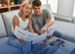 young couple sits on couch and looks over financials