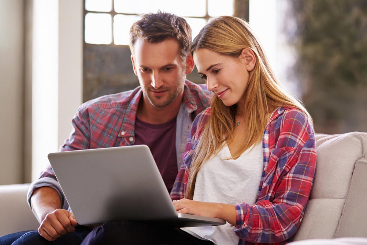 A couple sits together looking at a laptop, smiling as they review something on the screen.